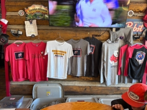 An array of custom t-shirts made by the Jackson Hole Alumni Chapter hangs on a wall.