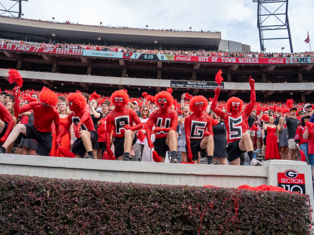 Several members of the paint line cheer on the Dawgs. Their bodies are painted red with black letters spelling out "DAWGS." 