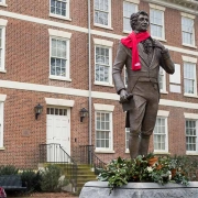 The Abraham Baldwin statue dressed with an Alumni Association scarf and a wreath of magnolia branches around the base of the statue for Founder's Week with Old College in the background.