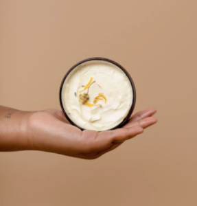 A hand holds up a container of Gently Soap Whipped Body Butter
