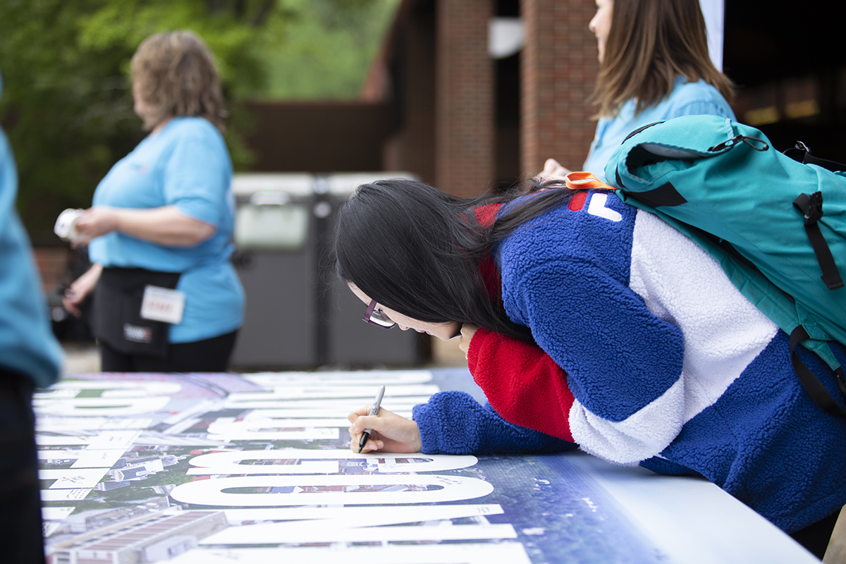 A student signs a banner dedicated to thanking donors.